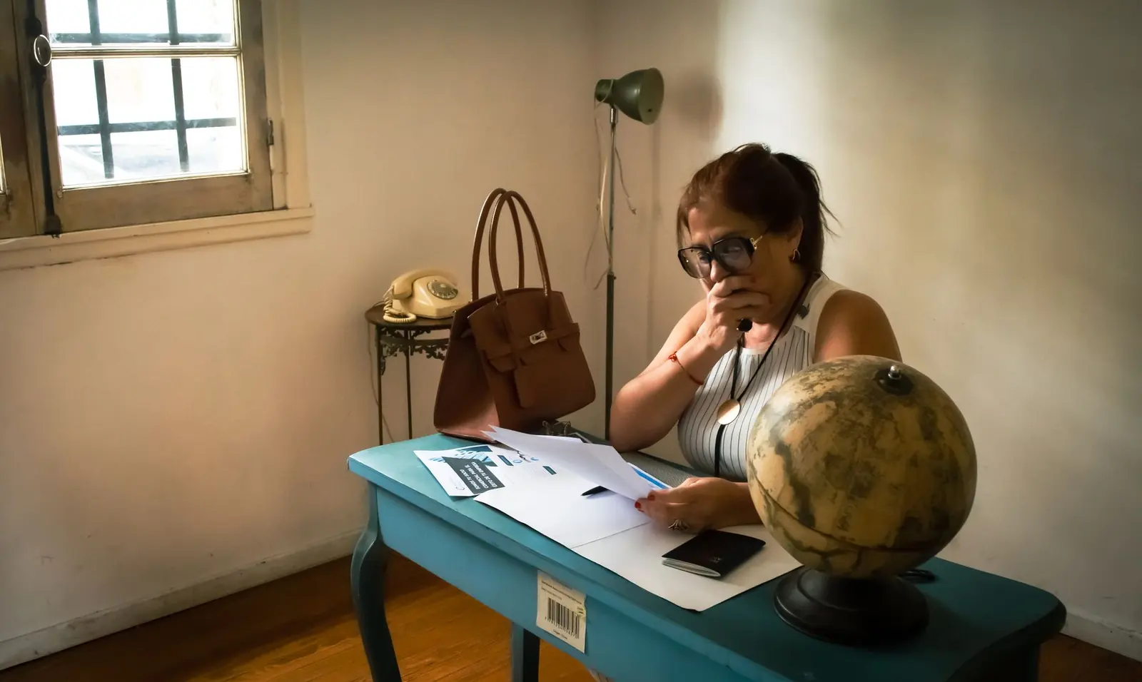 A woman working through paperwork at a desk in soft window light.